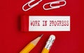 WORK IN PROGRESS message written under torn red paper with pencils and clips Royalty Free Stock Photo