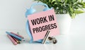 Work in Progress the writing on the sticky note near the blue alarm clock and colored pencils on the table. Royalty Free Stock Photo