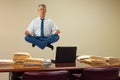 Work related stress relief with yoga as man hovering over stacks of paperwork and computer