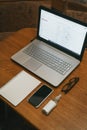 Work space with hand sanitizer laptop, notebook, glasses, pen, phone. Top view on dark wood table background. Remote work