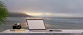 Work space with laptop mockup, camera, books and copy space on table with sunset beach view