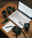 Work space photographer with laptop, digital camera, lenses, notebook, glasses, pen, phone and camera accessory. view on dark wood