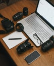 Work space photographer with laptop, digital camera, lenses, notebook, glasses, pen, phone and camera accessory. view on dark wood