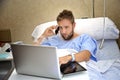 Workaholic business man in hospital room lying in bed sick and injured working with mobile phone computer laptop Royalty Free Stock Photo