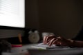 Workaholic hands typing keyboard in dark late night with computer screen light, clock, coffee cup and stuff on desk table with