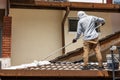 Worker adding undercoat foundation paint onto rooftop with roller at residential building in renovation