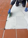 The worker applies the glue to a tile on a concrete floor