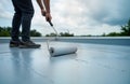 Worker applies waterproof coating on grey deck floor with paint roller. Construction site activity. Pro handyman repairs Royalty Free Stock Photo