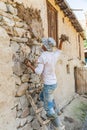 Worker applying mud plaster to a traditional stone house