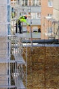 The worker assembles the scaffolding on the facade of a multi-storey house at a dangerous height