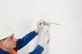 The worker attaches to the white wall the fasteners for hanging the cabinets of the kitchen furniture