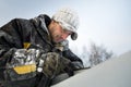 Worker in a black cap covered with frost sharpening a chainsaw chain