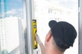 A worker in a blue headdress, with the help of a yellow level, checks the correct installation of the plastic window frame