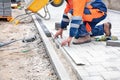 A worker uses a black marker and a straight aluminum batten to measure out a piece of paving slab for leveling on the sidewalk