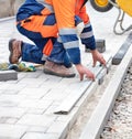 A worker measures a piece of paving slabs for leveling on the sidewalk. Vertical image