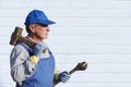 Worker in blue overalls with a sledgehammer and a wrench. Serious look. Against a white brick wall. Place for writing. Royalty Free Stock Photo