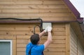 A worker in a blue uniform connects wires to electricity in the junction box of a wooden house