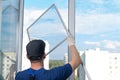 A worker in a blue uniform, rear view, installs a mosquito net in a plastic window frame, against the sky Royalty Free Stock Photo