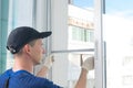 A worker in a blue uniform, rear view, removes a mosquito net from a plastic window frame, against the sky Royalty Free Stock Photo