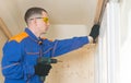 A worker in a blue uniform screws a wooden block to the concrete ceiling