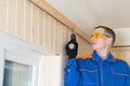 A worker in a blue uniform screws a wooden block to the concrete ceiling with a screwdriver, there is a place for the inscription