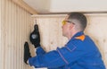 A worker in a blue uniform and yellow glasses screws a wooden block to the concrete ceiling