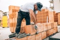 Worker building exterior walls, using hammer for laying bricks in cement. Detail of worker with tools and concrete