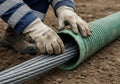 Worker carefully guides large electrical cable into protective green conduit underground Royalty Free Stock Photo