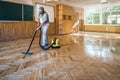 Worker carpenter cleans the parquet floor with professional vacuum cleaner. Industrial theme