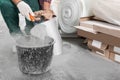 Worker with cement powder and trowel mixing concrete in bucket indoors, closeup