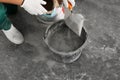 Worker with cement powder and trowel mixing concrete in bucket indoors, closeup