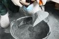 Worker with cement powder and trowel mixing concrete in bucket indoors, closeup