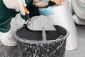 Worker with cement powder and trowel mixing concrete in bucket indoors, closeup