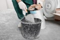 Worker with cement powder and trowel mixing concrete in bucket indoors, closeup