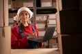 Worker checking inventory using Laptop Computer. Young female Santa Claus working in a warehouse with rows of shelves Royalty Free Stock Photo