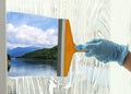 Worker cleaning window with squeegee, closeup. Picturesque river and mountains on sunny day, view through clear glass Royalty Free Stock Photo