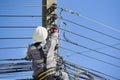 A worker climbs an electric pole to fix a broken wire wearing full safety harness.