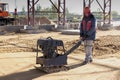 A worker compacts the earth with a vibrating rammer on a construction site on a bright sunny day. Preparation of the surface for