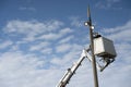 Worker conducts maintenance on a tall light pole using a lift beneath a clear blue sky with scattered clouds Royalty Free Stock Photo