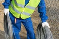 A worker in construction clothes carries a coil of iron wire