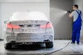 Worker covering automobile with foam at car wash.