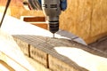 A worker drills a hole in a wooden bar with a drill on wooden. Wooden bar drilling with an electric drill. Construction background Royalty Free Stock Photo