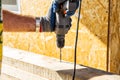 A worker drills a hole in a wooden bar with a drill on wooden. Wooden bar drilling with an electric drill. Construction background Royalty Free Stock Photo