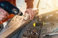 A worker drills a hole in wooden bar with drill