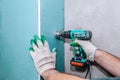 A worker drills holes in a plasterboard wall with an electric drill. Repair in the house