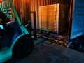 Worker driving forklift loading shipment carton boxes goods on wooden pallet at loading dock from container truck to warehouse