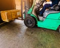 Worker driving forklift loading and unloading shipment carton boxes and goods on wooden pallet from container truck to warehouse c
