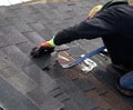 ROOFING: Worker examines damaged shingles.