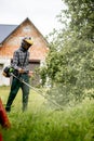 Worker with a gas mower in his hands, mowing grass in front of the house. Trimmer in the hands of a man. Gardener cutting the Royalty Free Stock Photo