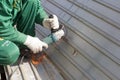 Worker in green uniform and in rags gloves grinds corrugated steel structure for painting primer anti rust.